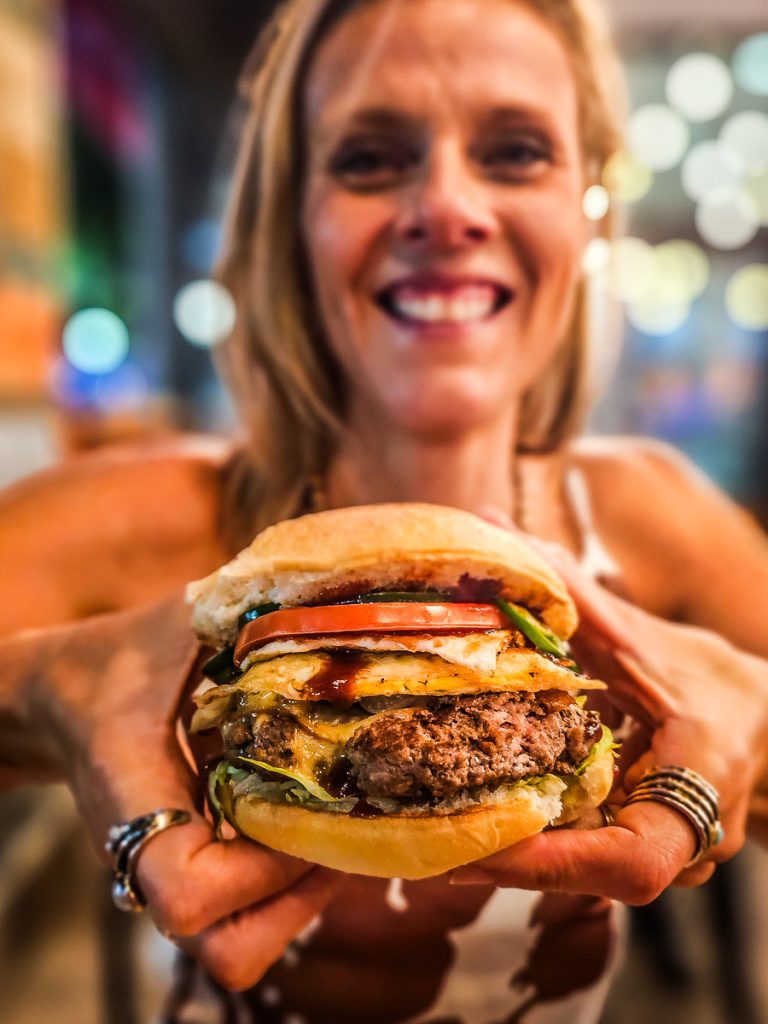 Woman holding up a burger in her hands and smiling.