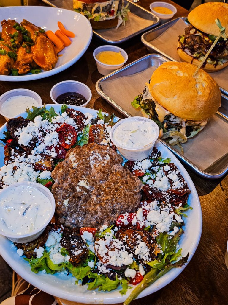Salad with a lamb patty on top, plus a burger and chicken wings.