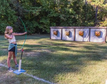 savannah pulling back on bow and arrow on archery field