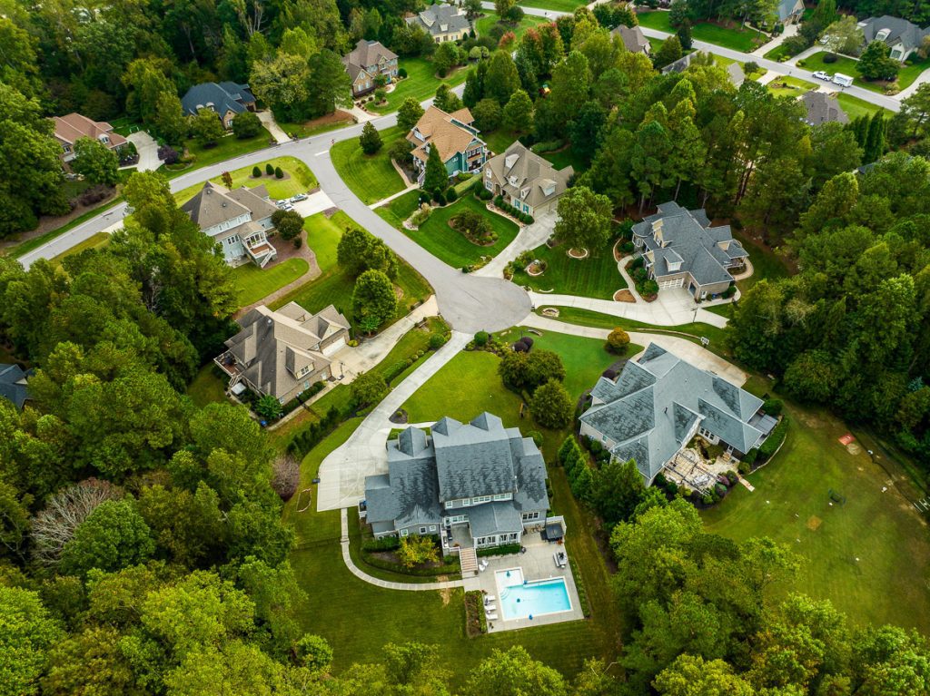 Aerial photo of houses in a neighborhood with green trees and a pool.