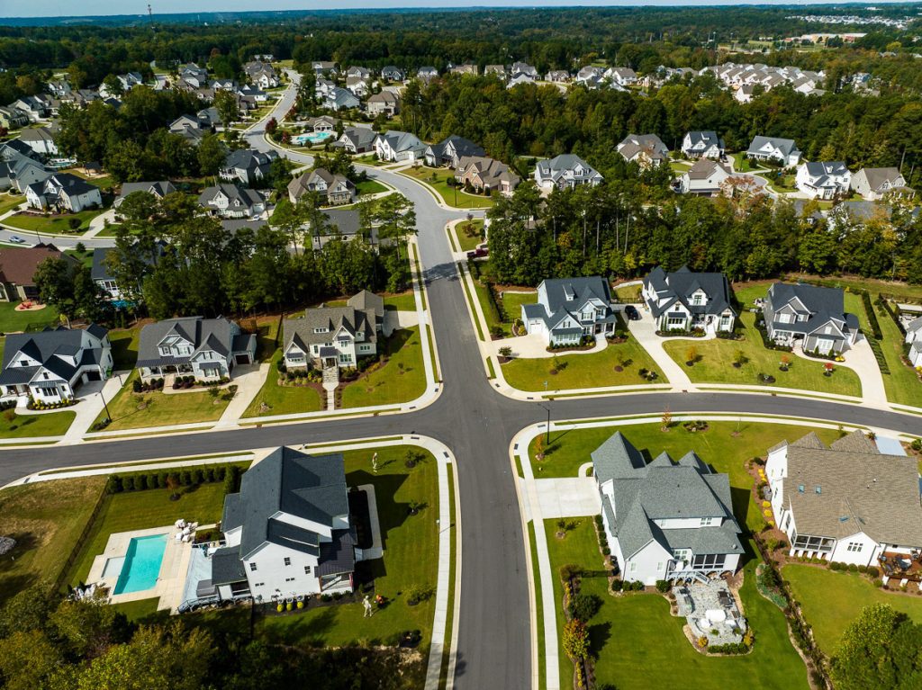 Aerial photo of houses in a neighborhood with green trees and a swimming pool.