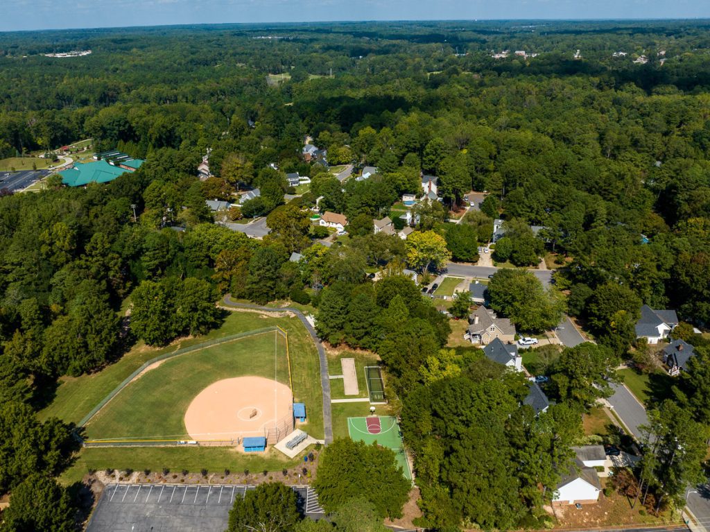 Aerial photo of a neighborhood with green trees and a baseball field.
