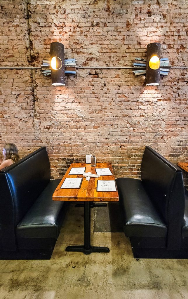 Table and booth in a restaurant with brick wall and lights in background.