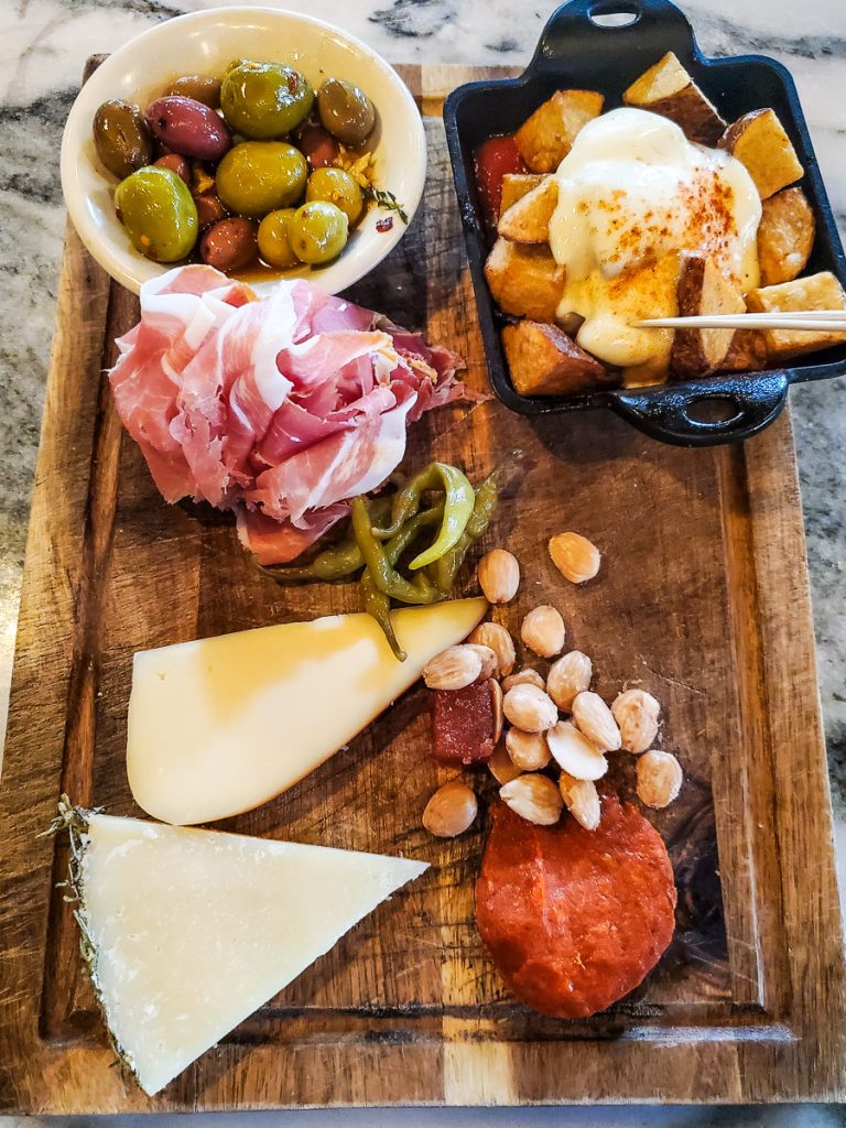 Charcuterie board of cheeses, olives, meats, nuts, and potatoes.