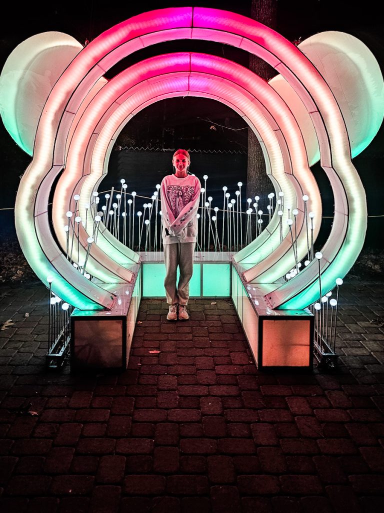 Young girl standing under a light display.