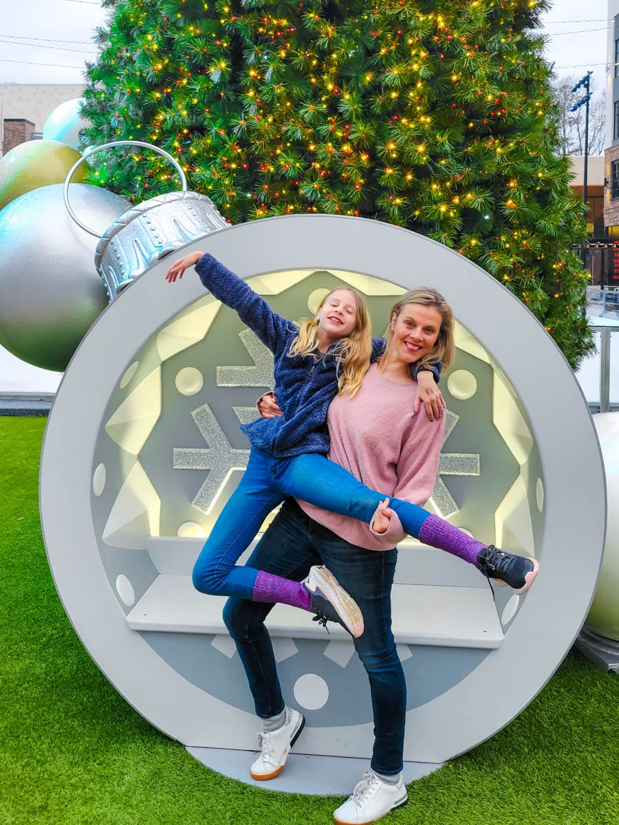 woman holding girl in front of giant christmas ornament and tree