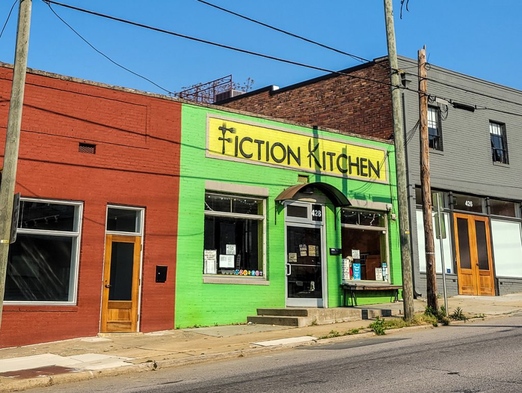 Exterior of a vegetarian restaurant painted green with the words Fiction Kitchen.