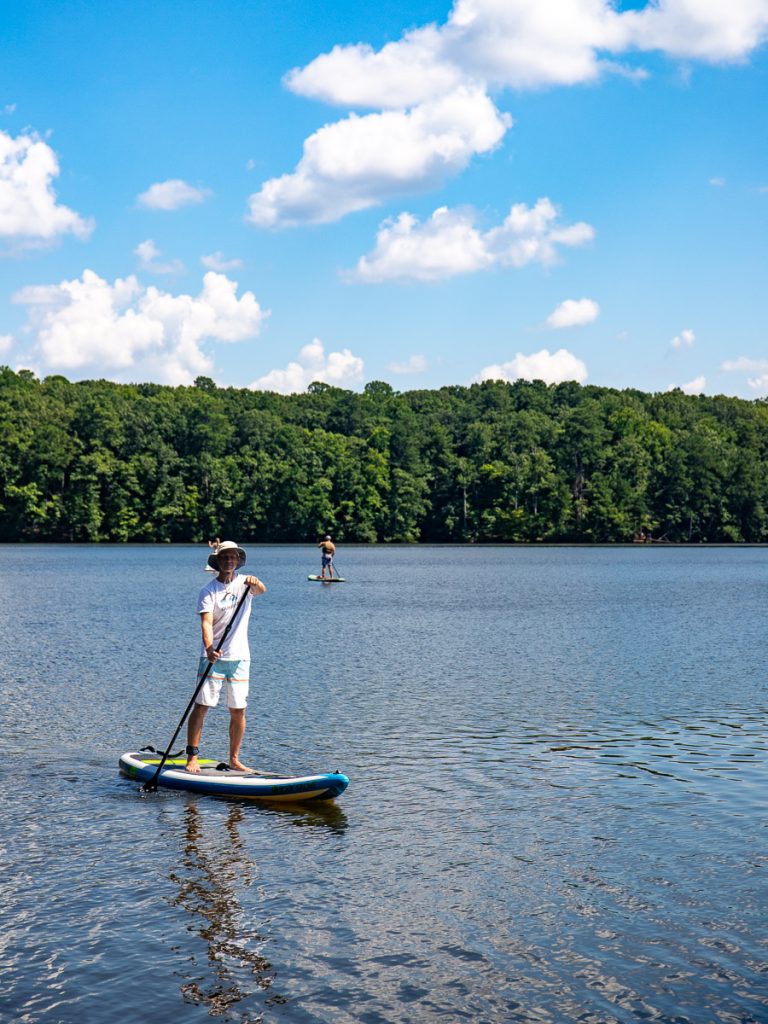Man on a paddle board on a lake surrounded by trees.