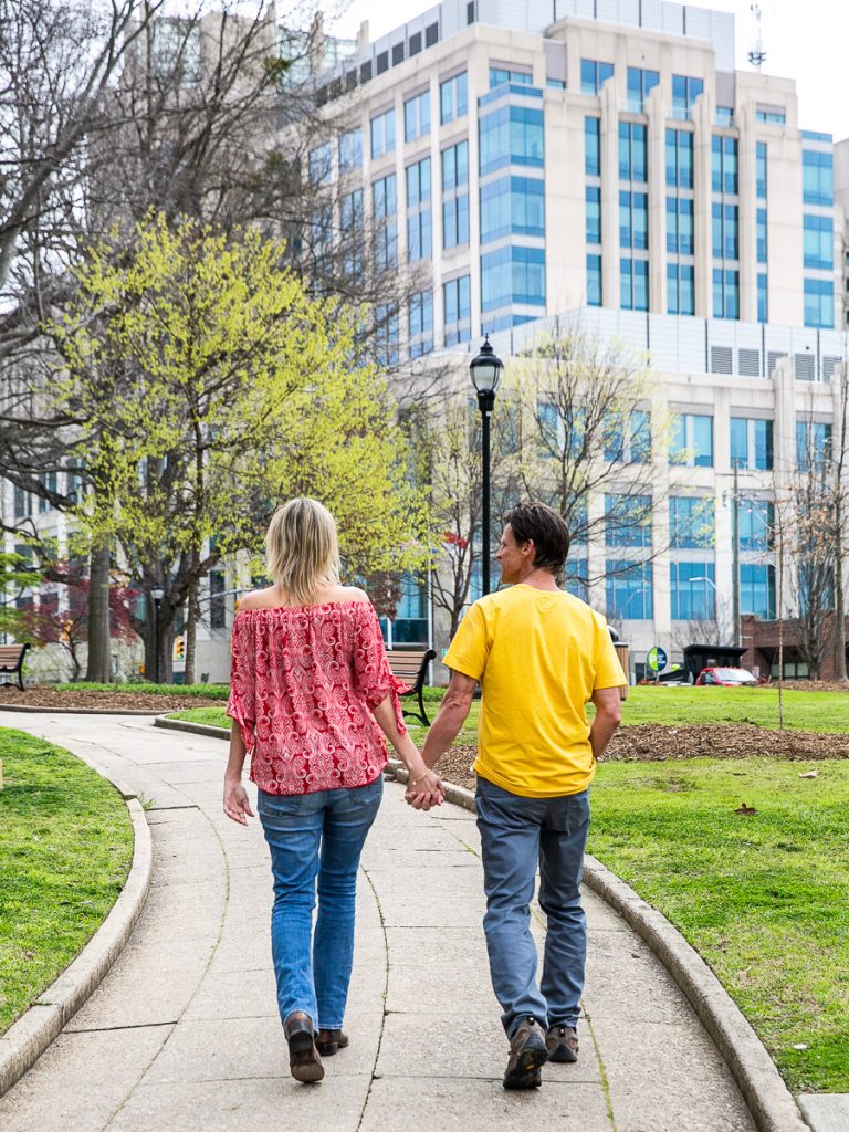 Man and woman holding hands walking through a city park.