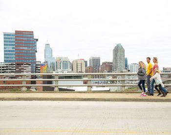 Family of four walking across a bridge with city buildings in the background.